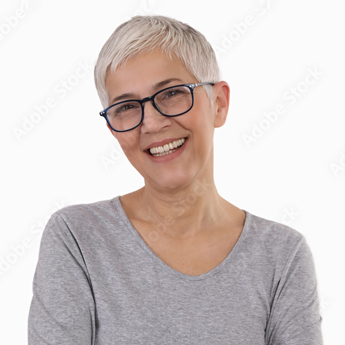 Middle-aged woman with white hair, dark-rimmed glasses and a light gray shirt smiling