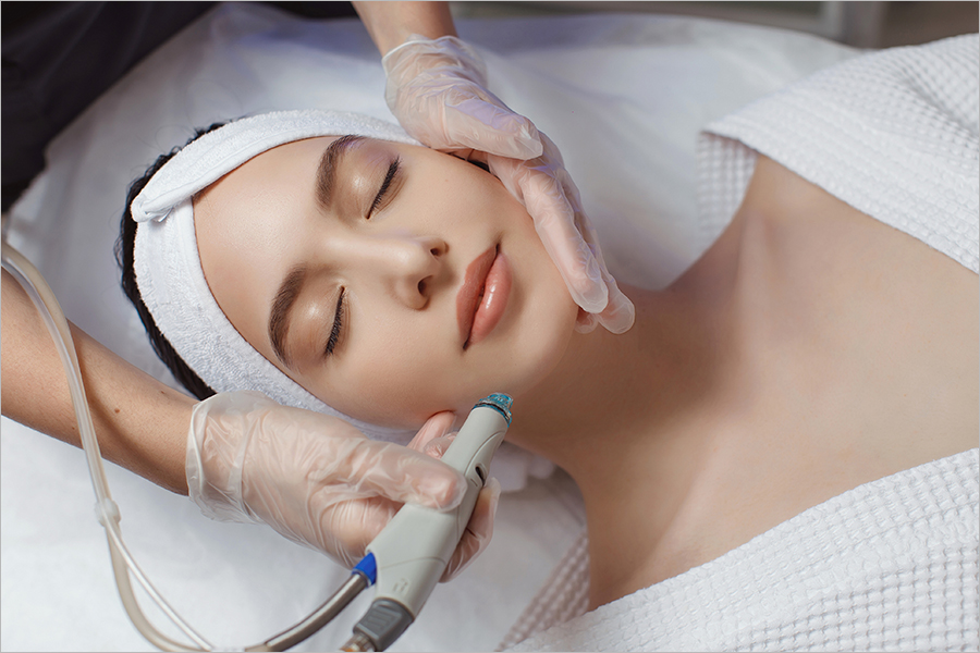 Side view of woman receiving microdermabrasion therapy on forehead at beauty spa. Hydradermabrasian procedure in Cosmetology clinic.