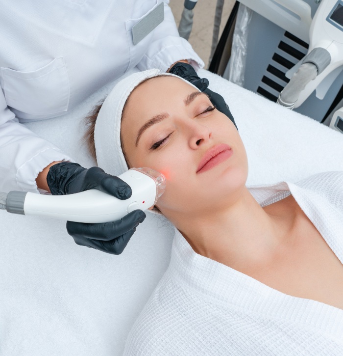 Woman in white robe and headband with eyes closed receiving microneedling treatment with radiofrequency